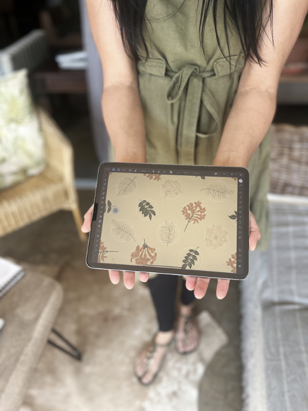 Martie Erasmus ina green dress in her home showing her ipad with a seamless repeat pattern of the Cape Honeysuckle pattern that is available for licensing.