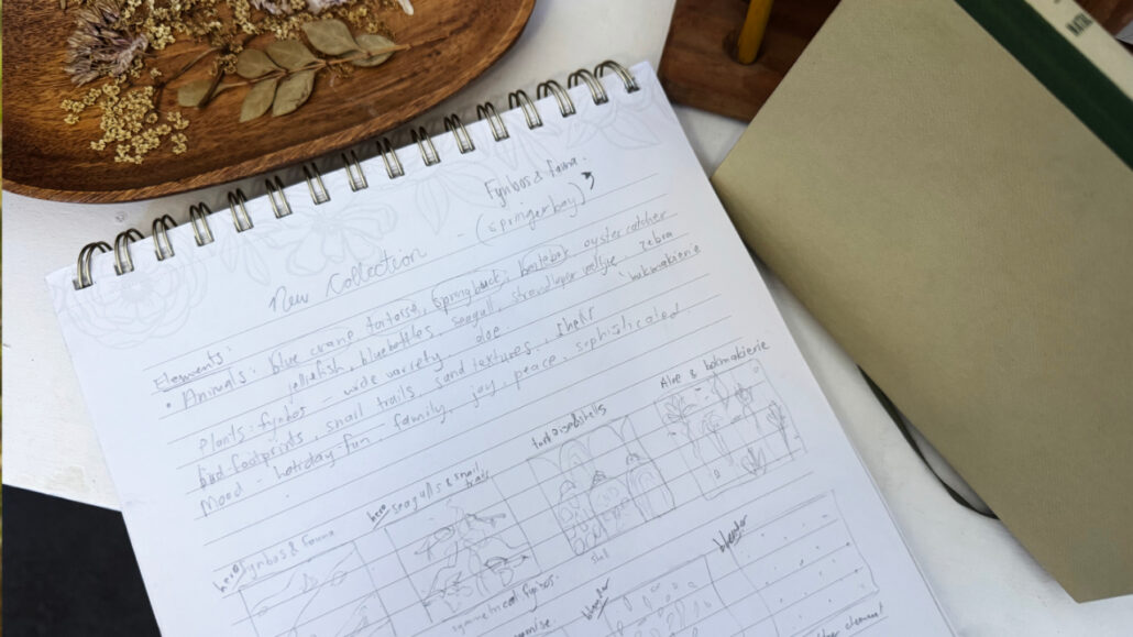 Artist Martie Erasmus' coiled planner with Brainstorming notes on a new collection - she mapped out the story and thumbnails for the seamless repeat patterns. Next to the notebook is a wooden tray with dried flowers and leaves and a little vintage book on the FLowers of Natal as inspiration.